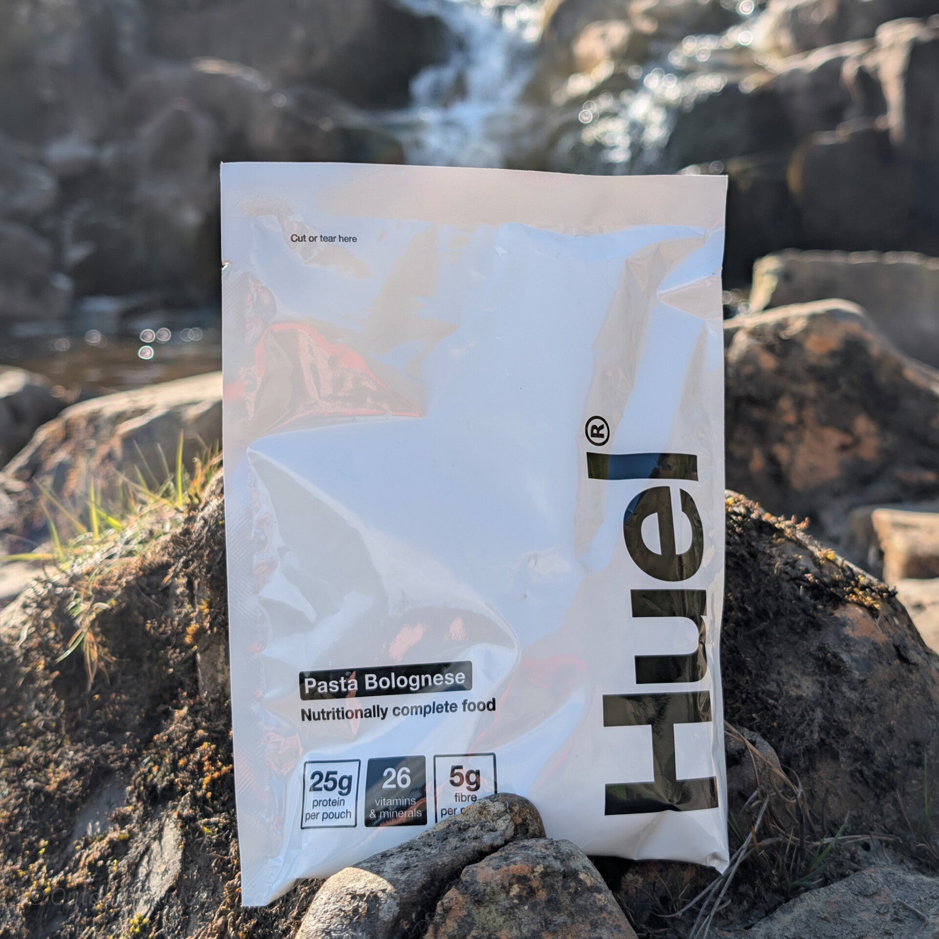 Huel hot and savoury meal pouch placed near a waterfall during a walk