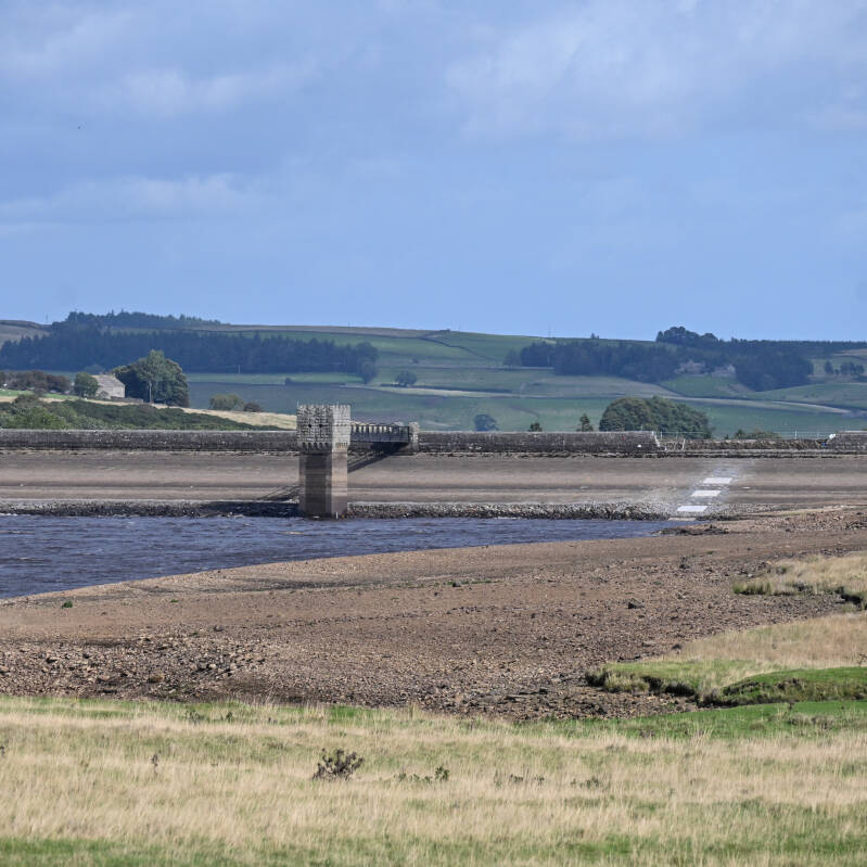 Wide view across the exposed reservoir bed towards the dam and tower at Hury Reservoir during the 2026 drawdown