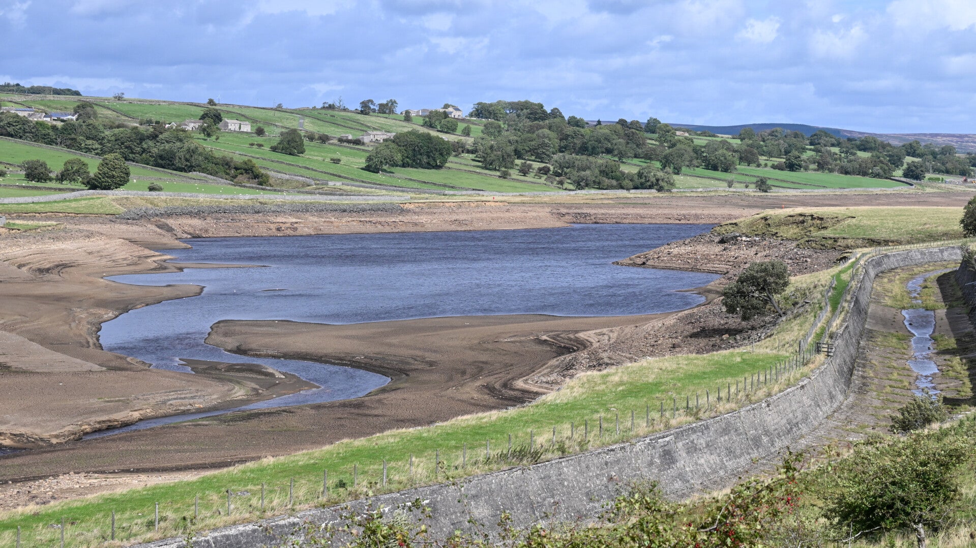Wide view across Hury Reservoir showing the dramatically lowered water level and exposed reservoir bed during the 2026 drawdown