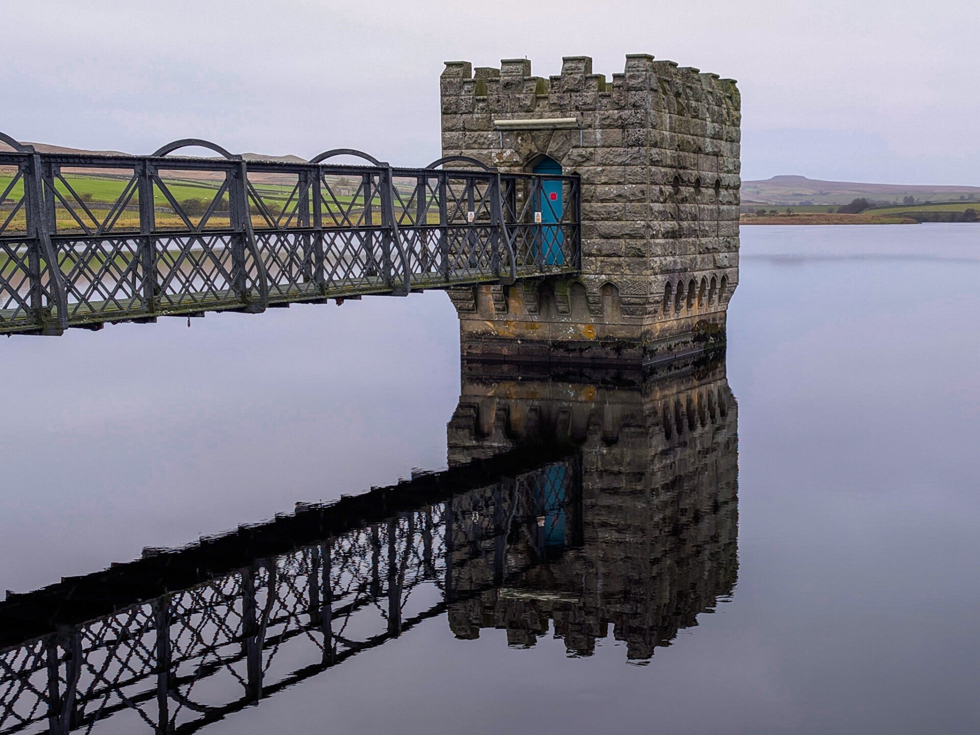 Valve tower and metal footbridge reflected in the calm water of Hury Reservoir in Baldersdale