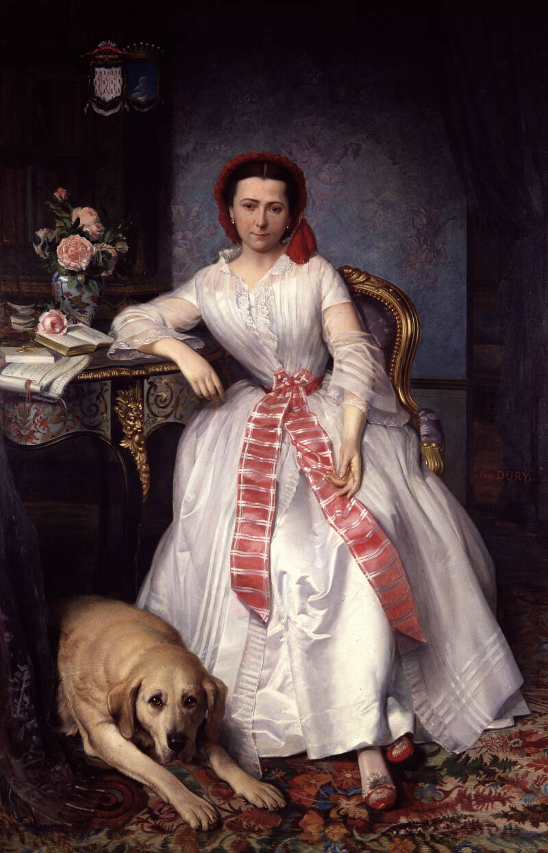 Photograph of a classical-style painting depicting a woman seated on an ornate chair wearing a white dress with a red sash and headscarf, accompanied by a large dog lying on a patterned carpet. The setting includes a decorative table with flowers, books, 
