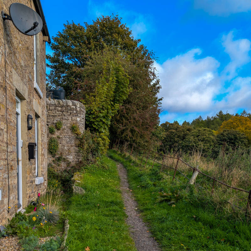 Narrow footpath beside stone cottages at Hude, leading towards the King's Walk woodland in Middleton-in-Teesdale.