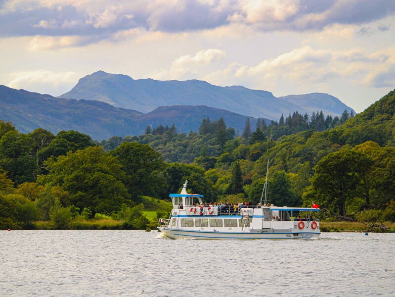 A peaceful boat on a Lake District lake surrounded by trees and distant mountains