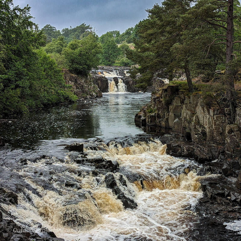 Downstream perspective of Low Force showing layered cascades, dark rocks and the river winding through the Teesdale gorge.
