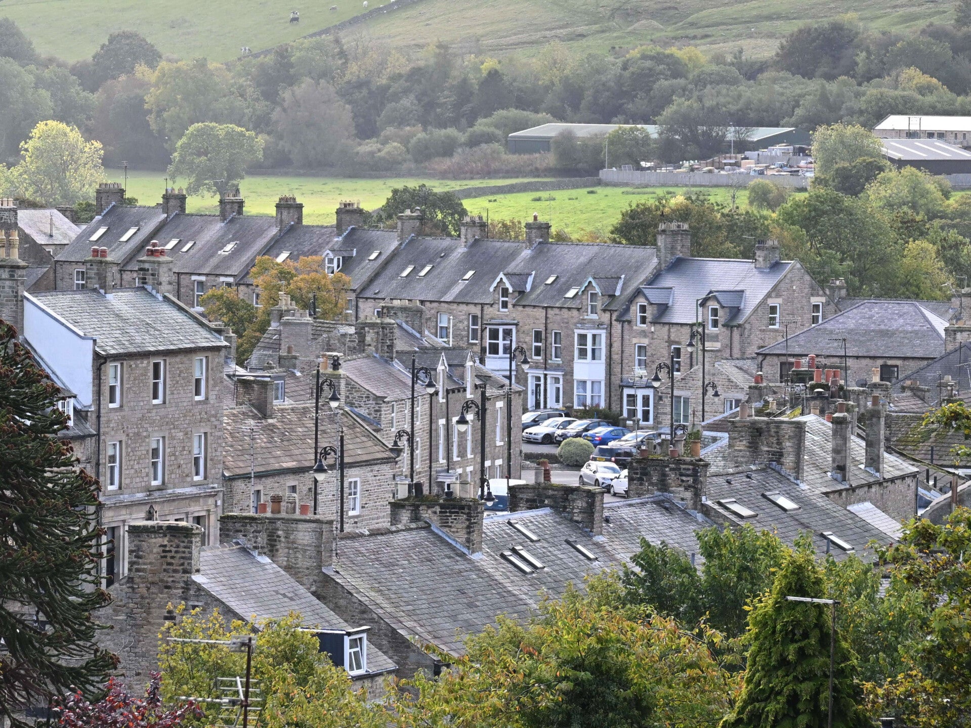 View across the stone rooftops, terraced houses and Market Place of Middleton-in-Teesdale, with green fields and wooded hillsides beyond the village.