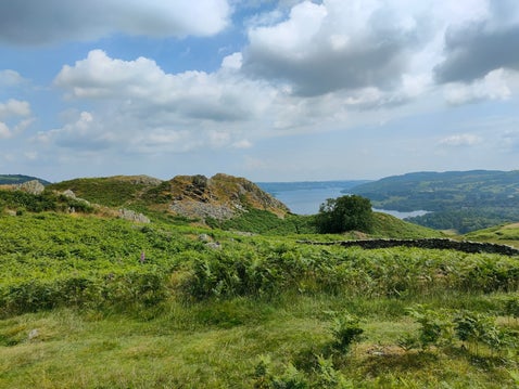 View across the Lake District fells from the Todd Crag walk near Ambleside, with rocky crags, green bracken and Windermere in the distance.