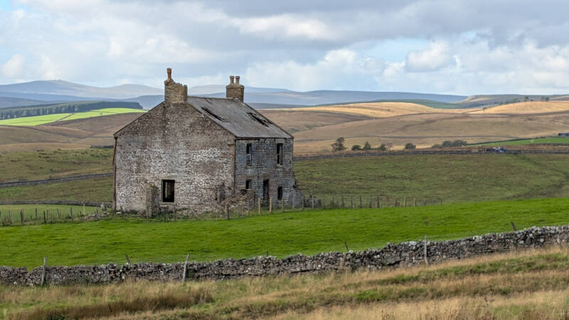 Front of Red Grooves House, an abandoned stone farmhouse near Middleton-in-Teesdale, with a damaged slate roof, empty windows and two chimneys.