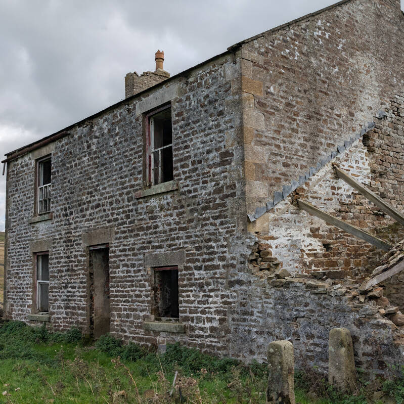 Side of the abandoned Red Grooves farmhouse in Teesdale, with old sash windows, stone walls and the collapsed remains of an attached farm building.
