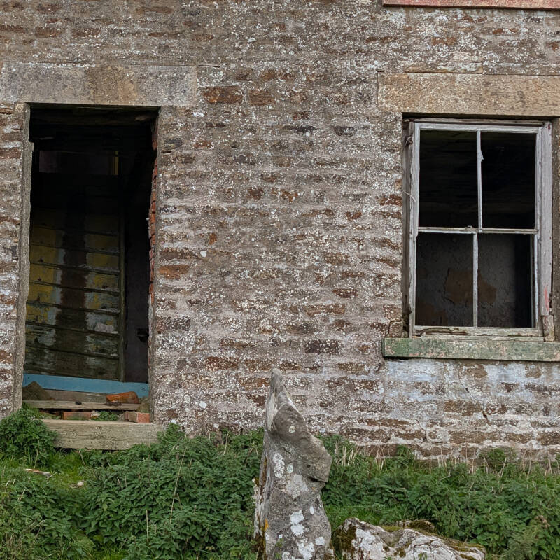 Close-up of the empty doorway and surviving wooden sash window at Red Grooves House above Newbiggin, showing the old stonework.