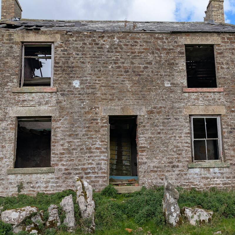Front wall of the derelict Red Groves farmhouse in Upper Teesdale, showing five window and door openings, damaged roof slates and surviving stonework.