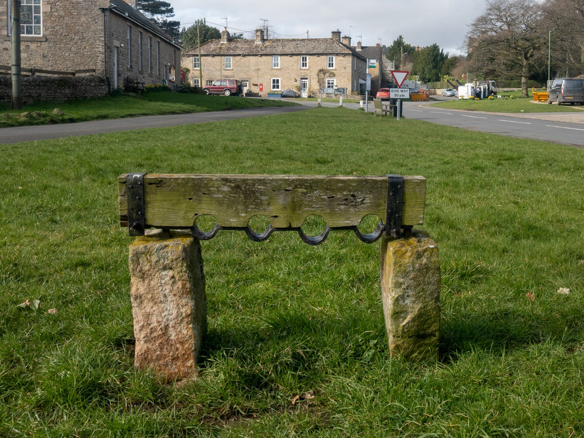 Historic village stocks on Romaldkirk green in Teesdale, showing wooden restraint frame with stone supports and surrounding cottages