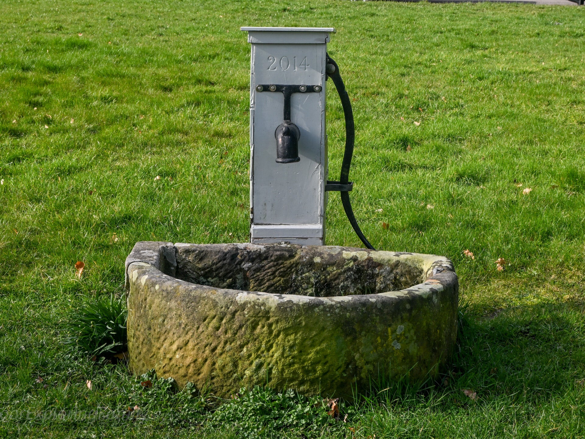 Historic water trough and hand pump on Romaldkirk village green in Teesdale, showing stone basin and restored metal pump