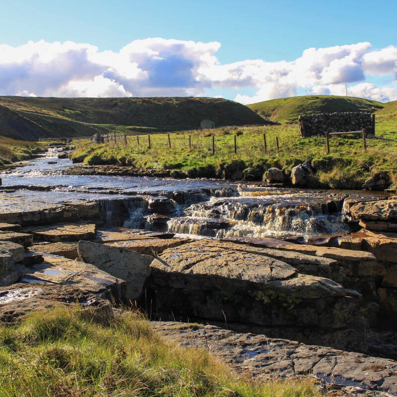 Upper section of Sleightholme Beck with a series of small waterfalls and bright moorland scenery.