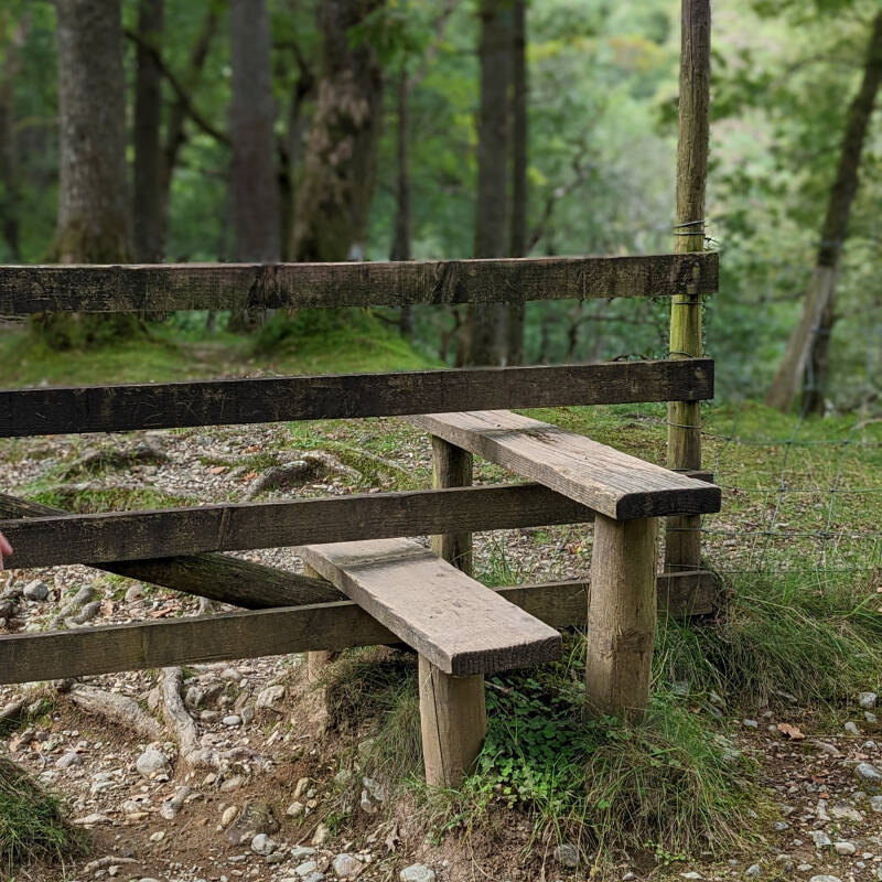 Wooden stile leading into Castle Crag woodland, marking the transition from open paths into forest.