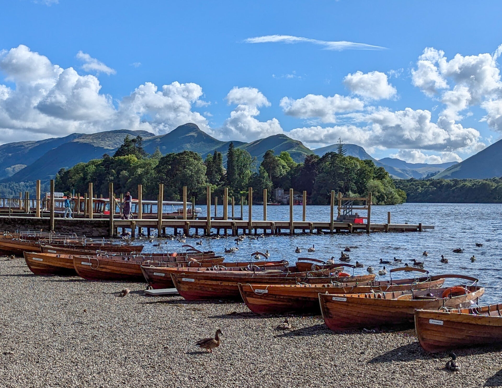 Rowing boats on a lakeshore with Lake District mountains in the background