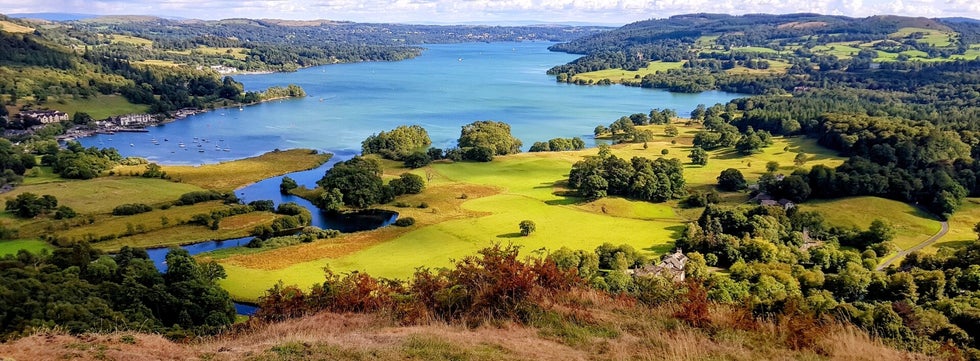 Panoramic view over Lake Windermere from Todd Crag near Ambleside, showing green fields, woodlands and boats on the water in the Lake District.
