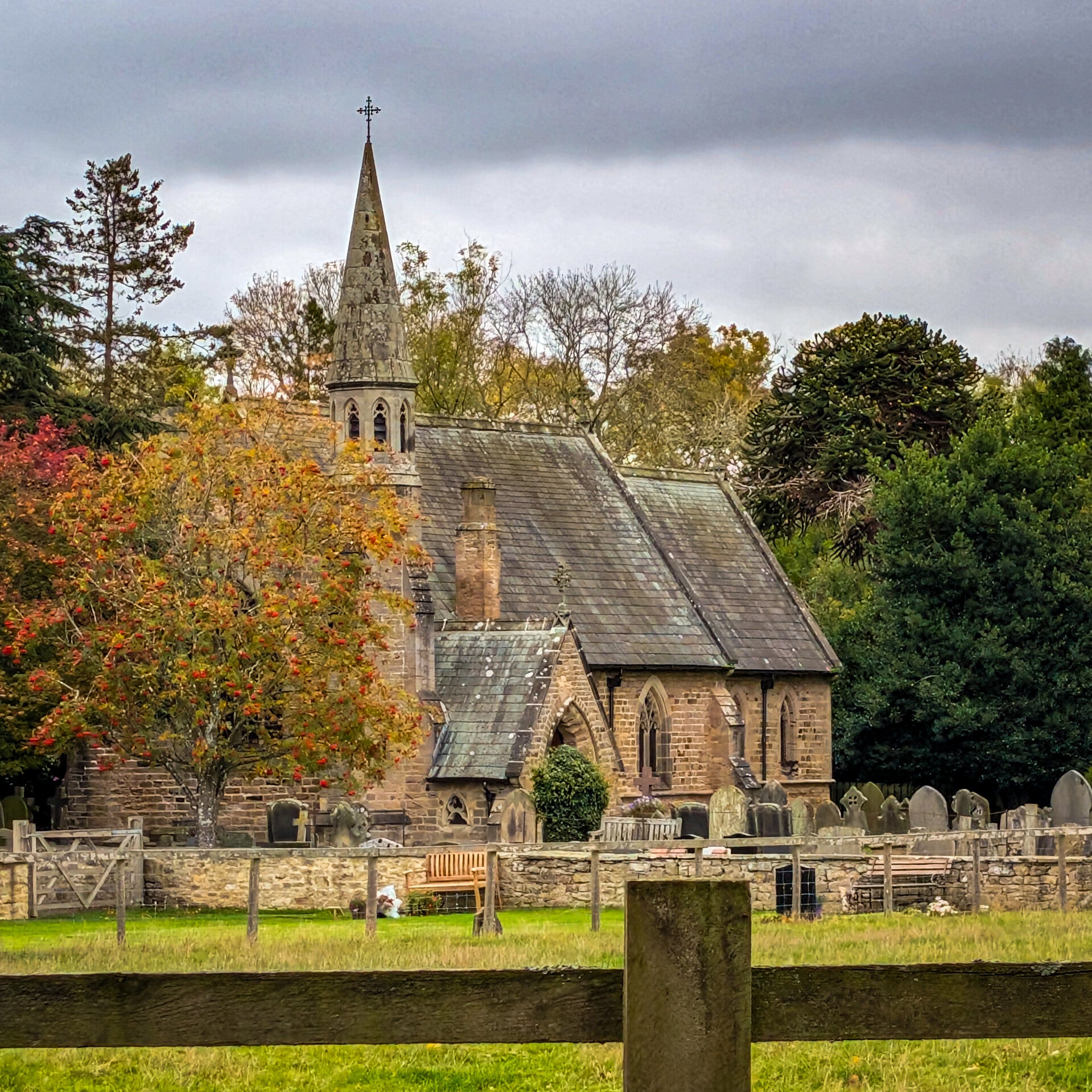 St Mary's Church in Whorlton, with its stone spire, historic graveyard and surrounding autumn trees.