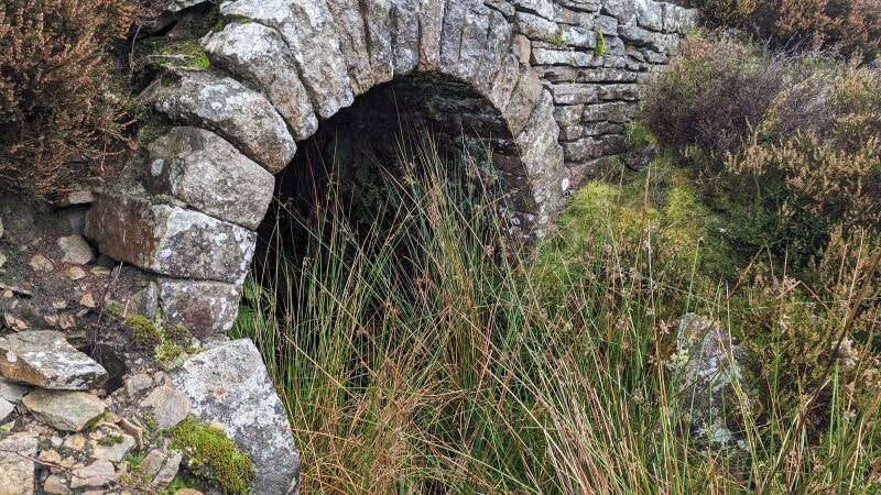 Entrance to an old lead mine near Great Eggleshope Beck, with stone walls and grassy moorland around it in Upper Teesdale.