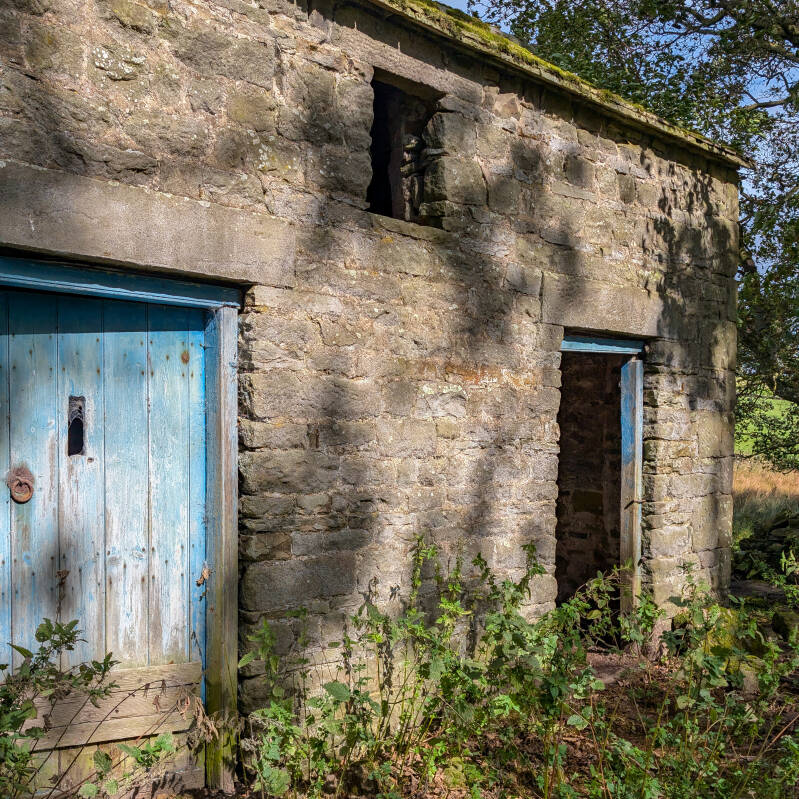 Old stone farm building with a weathered blue door at Yew Tree Farm near Hury Reservoir
