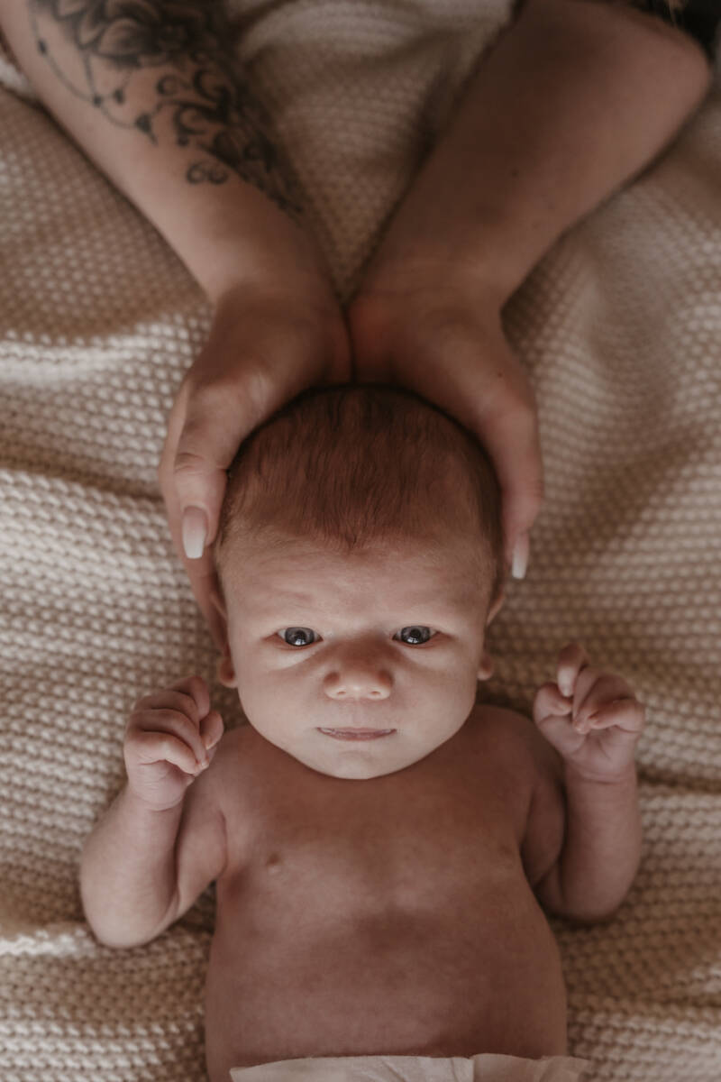 Newbornshoot slaapkamer bed thuis baby handen details warm