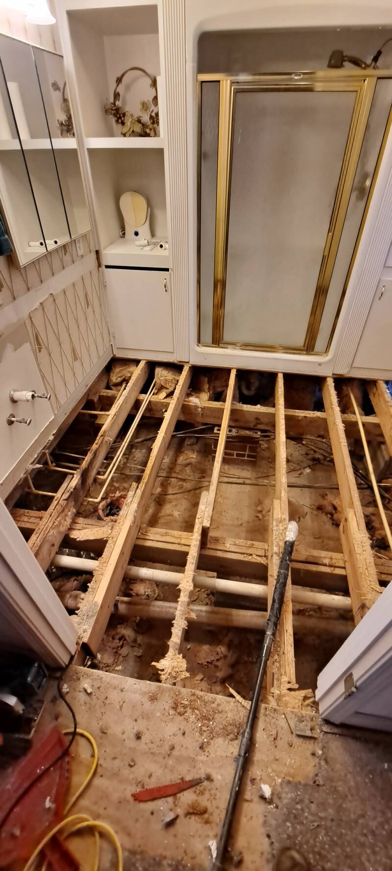 Bathroom remodel before photo showing complete floor tear-out down to exposed joists due to water damage, preparing for subfloor replacement and full renovation by New Looks 4 Home LLC in Upstate South Carolina.