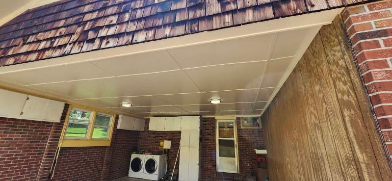 Completed garage ceiling renovation with smooth finished panels and recessed lighting installed above brick walls.