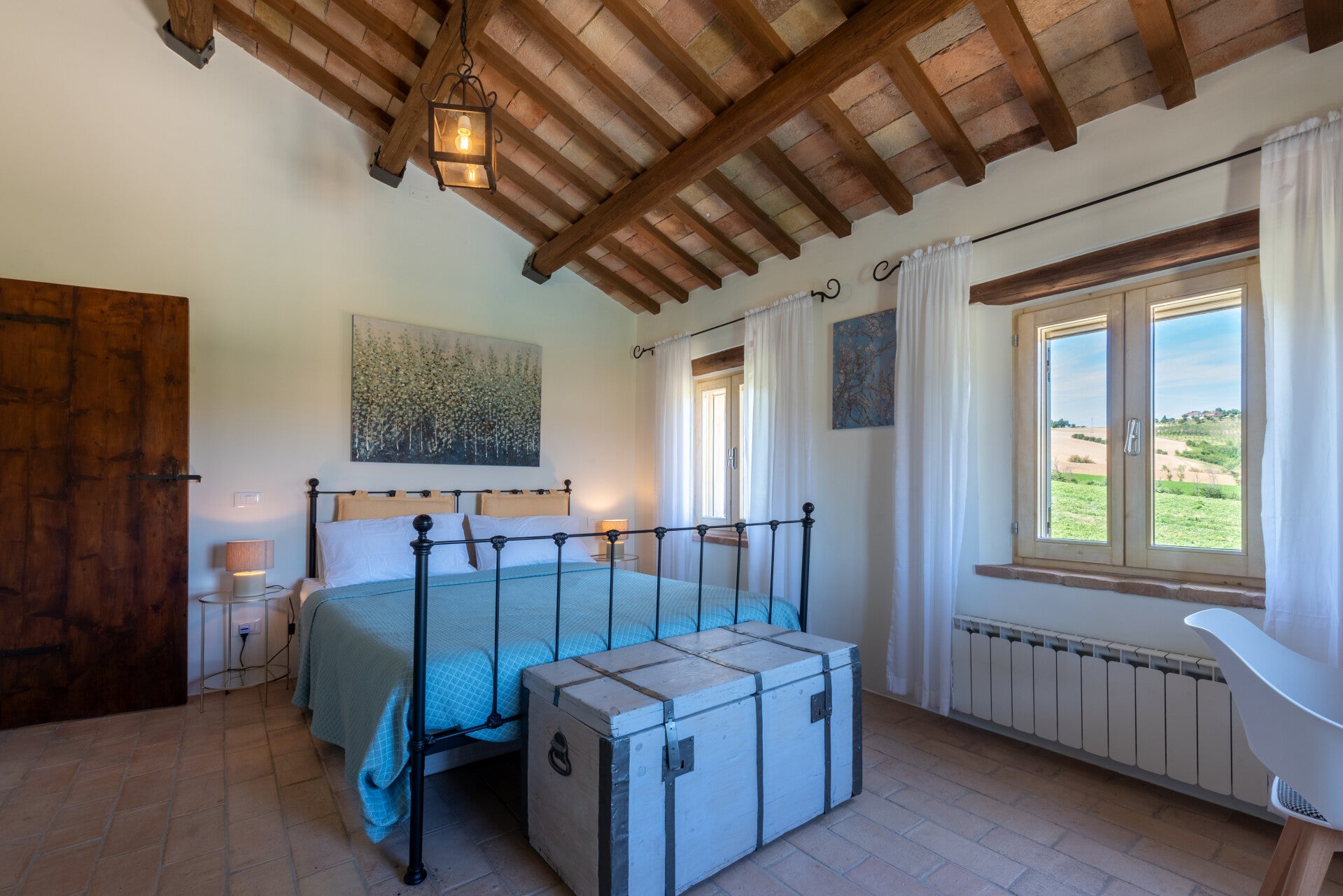 Beautiful upstairs bedroom boasts striking exposed wooden beams, classic terracotta floors, and a wrought-iron double bed