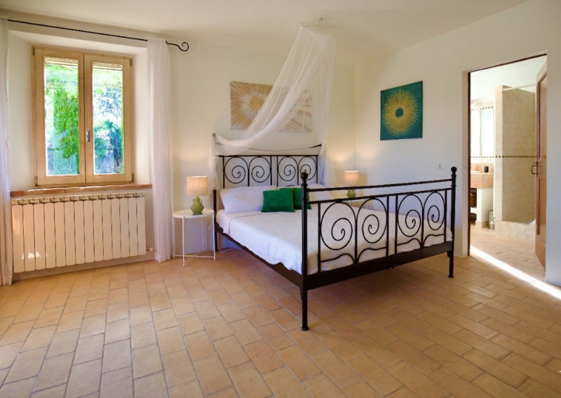 Inviting ground-floor bedroom features a stunning wrought-iron bed frame with a delicate canopy accent, classic tile flooring, and a sunlit garden view