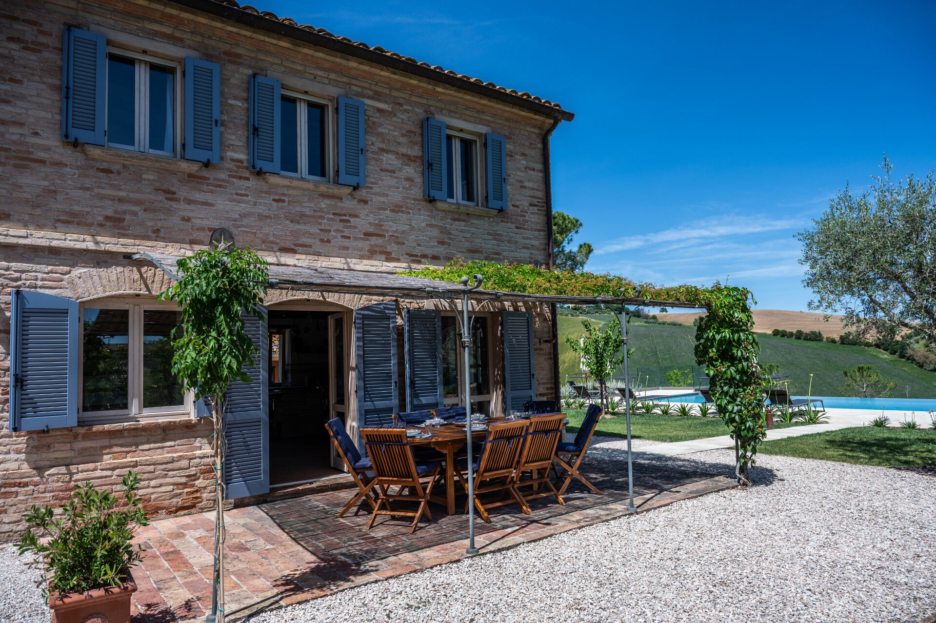 East facade of Casale Oleandri showing one of the two outdoor dining areas and the white gravel path leading to the pool