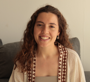Retrato de una mujer joven, sonriendo, sentada en un sillón, con chaqueta clara de bordados