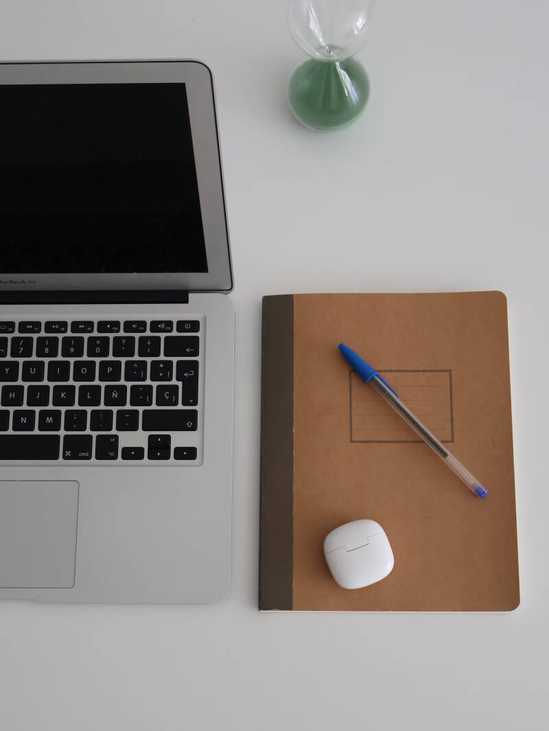 Ordenador con cuaderno marrón, bolígrafo azul y funda blanca de auriculares