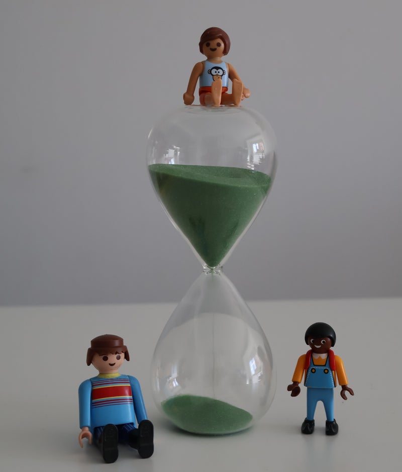 Tres muñecos play movil, dos a los lados de un reloj de arena verde y otro sobre él
