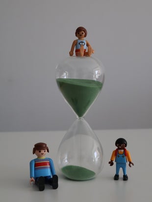 Tres muñecos play movil, dos a los lados de un reloj de arena verde y otro sobre él