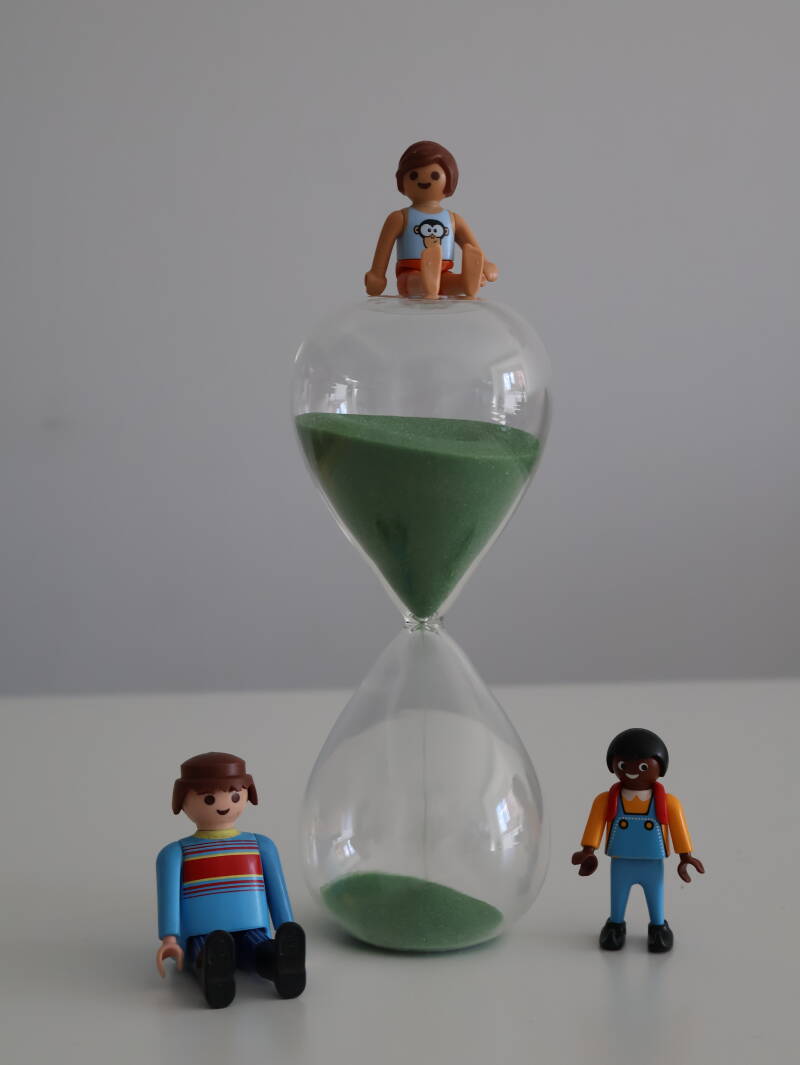 Tres muñecos play movil, dos a los lados de un reloj de arena verde y otro sobre él