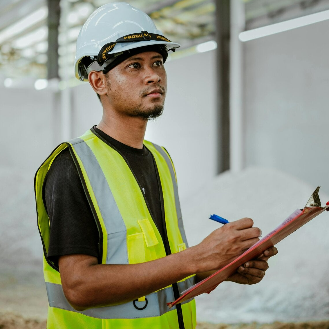 A health and safety manager in a high-vis jacket writing on a clipboard.