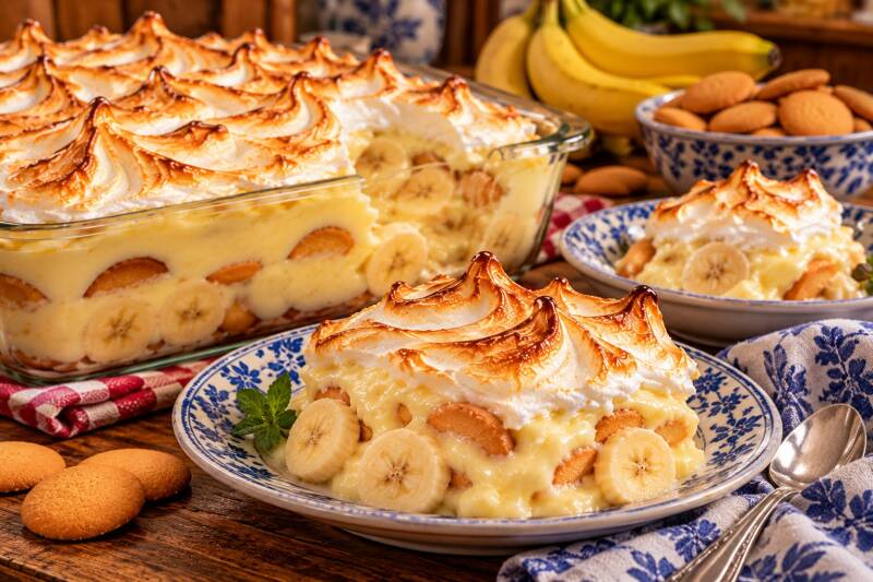 Old fashioned banana pudding with toasted meringue, sliced bananas, and vanilla wafers in a baking dish and on a plate