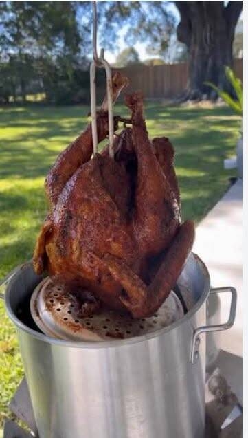 Crispy Cajun fried turkey lifted out of propane turkey fryer in backyard, golden brown Thanksgiving turkey recipe