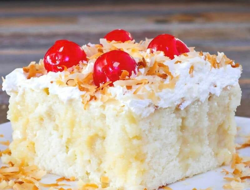 Close-up slice of Mama’s Famous Coconut Poke Cake with whipped Cool Whip frosting, toasted coconut, and maraschino cherries on white plate, moist Louisiana church cookbook recipe from Ponchatoula, LA, @NanaTeesCajunHome