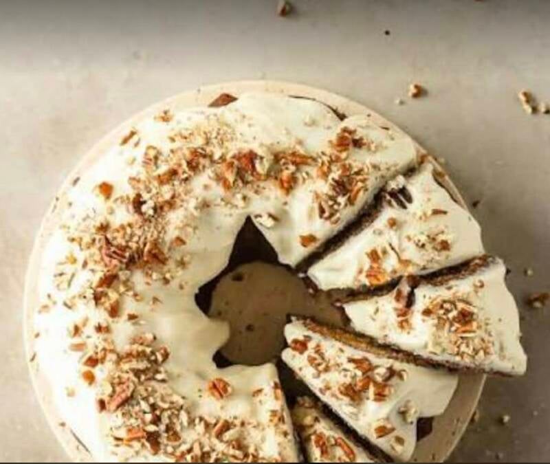 Overhead view of sliced Aunt Juanita’s carrot bundt cake with maple cream cheese frosting and chopped pecans on white cake stand, Louisiana recipe from Manchac, @NanaTeesCajunHome