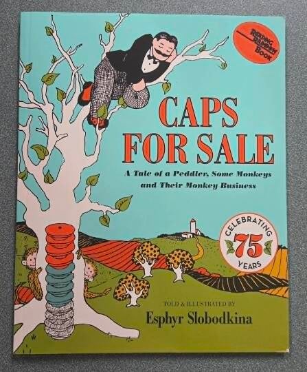 Caps for Sale 75th Anniversary Edition book cover by Esphyr Slobodkina. Turquoise background shows peddler sleeping in tree with stack of red, blue, gray caps on his head. Monkeys in branches. Reading Rainbow Book. Educational gift for grandkids.