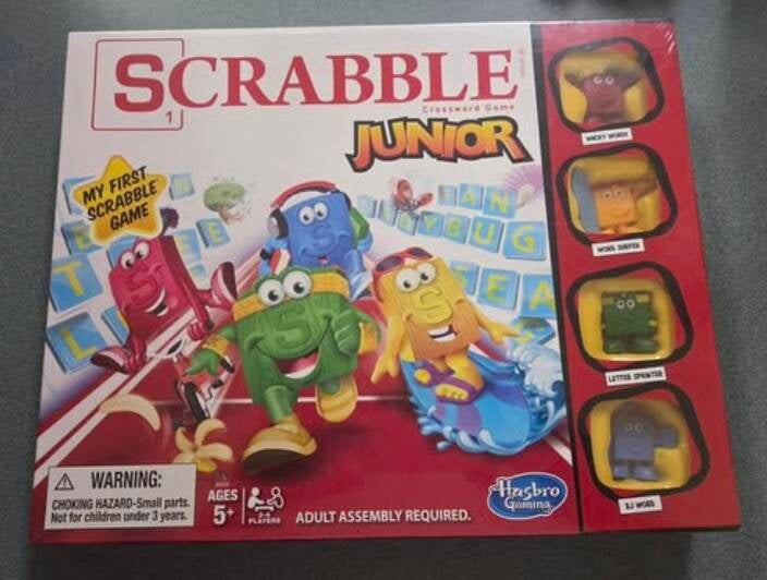 Scrabble Junior board game box by Hasbro. Cover shows colorful letter characters racing. Includes Wacky Wordy, Word Surfer, Letter Sprinter, DJ Word tokens. My First Scrabble Game for ages 5+, 2-4 players. Educational gift for grandkids.