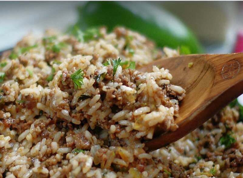 Authentic Cajun dirty rice with ground beef and pork in cast iron skillet served with wooden spoon and sprinkled with parsley