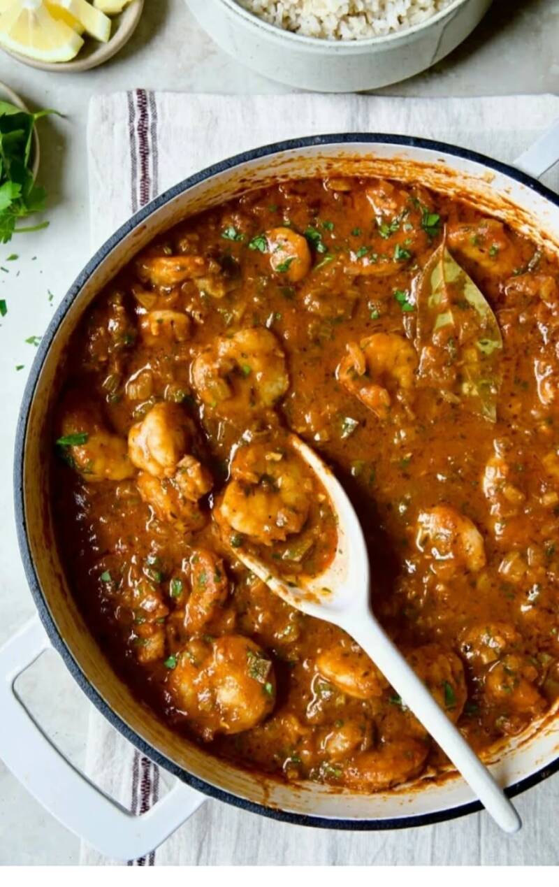 Shrimp creole simmering in a white Dutch oven with bay leaf and fresh parsley