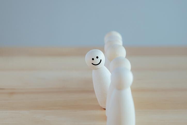 Mehrere weiße Spielfiguren stehen in einer Reihe, die vorderste trägt ein lächelndes Gesicht, im Kontext mit Jenseitskontakte Jana Lorenz - Podcast.