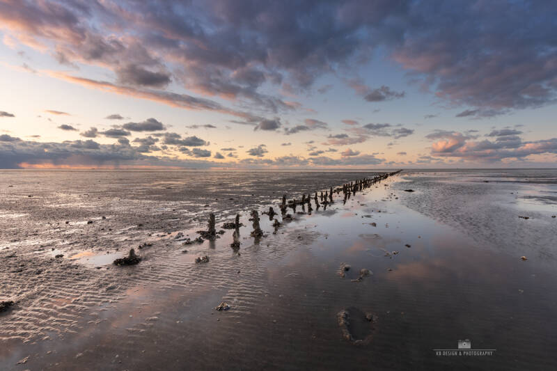 paaltjes in het slik, van de Waddenzee bij Wierum. Wolken worden weerspiegeld boven het water