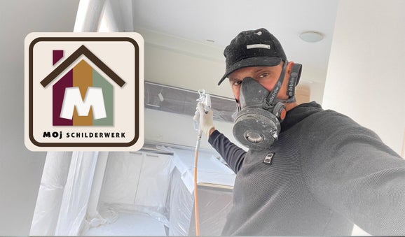 Schilder met spuitkop in hand tijdens voorbereidend spuitwerk, keuken volledig afgedekt met plastic ter bescherming
