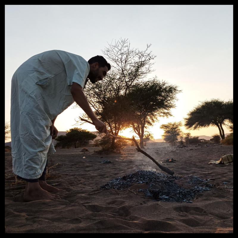 Mann bereitet frisches Sand-Brot in der Glut eines Lagerfeuers zu