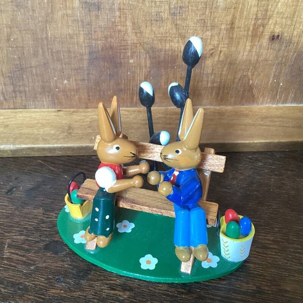 Ertsgebergte hazen echtpaar op bank met emmers met eitjes en voorjaarstakken 11 cm hoog, 10 cm breed
