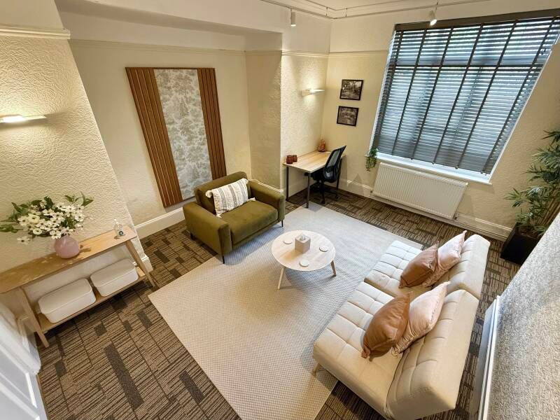 Overview of Calm Place Therapy Room. The room features an olive green arm chair, neutral sofa as well as a working desk space and calming decor. 