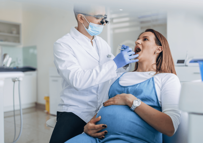 Dentista realizando una revisión bucodental a una mujer embarazada durante una consulta odontológica. 